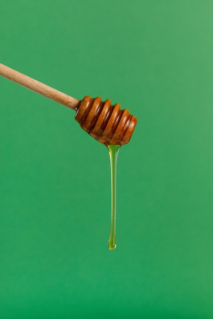 Honey flowing dripping from wooden dipper stick over green background