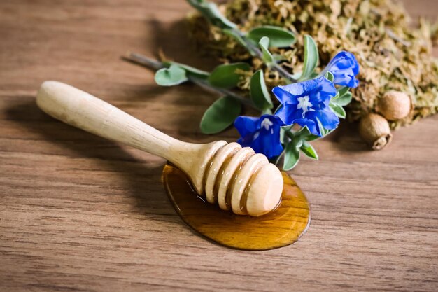 Honey flows from a honey dipper on wooden table and a little blue flower  on wooden table