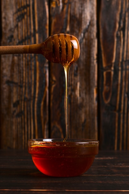 Honey flows from a stick into a jar. Rustic sweet photo, wooden background, copyspace.