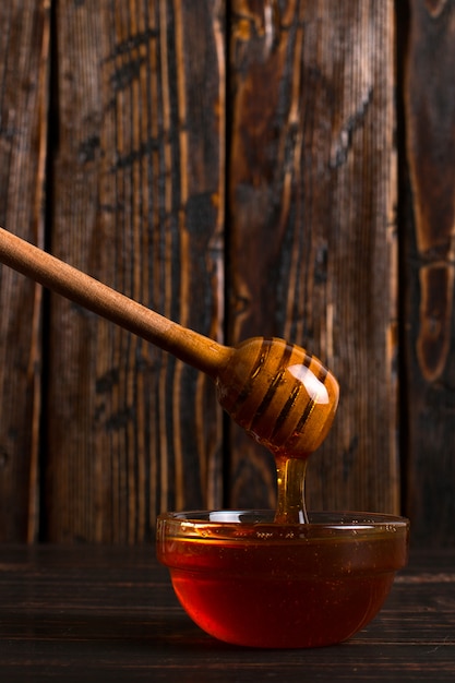 Honey flows from a stick into a jar. Rustic sweet photo, wooden background, copyspace.