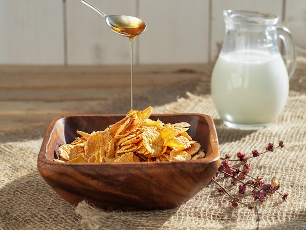 Honey from a spoon is poured into corn cereal and jug of milk