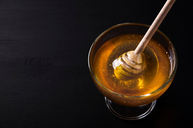 Honey in a glass bowl  honey dipper on a dark background. Space for text.