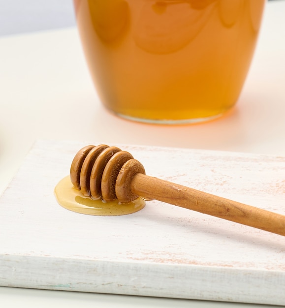 Honey in a glass transparent jar and a wooden stick on a white table, top view