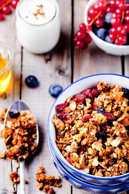 Honey glazed oatmeal nut and flax seeds granola in a ceramic bowl with honey yogurt and fresh berries on a wooden background