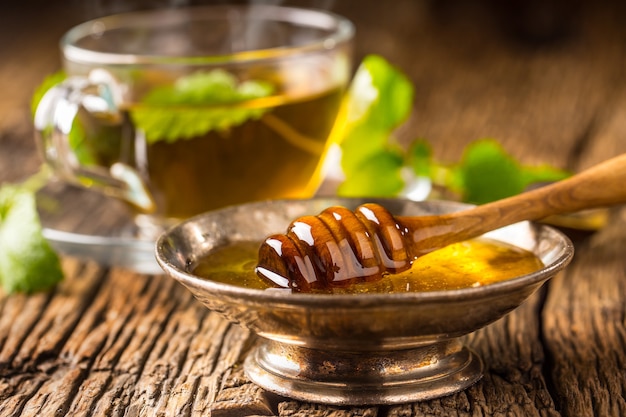 Honey. Honey and honey dipper on rustic oak table. Hot herb tea in the background.