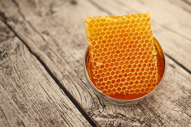 Honey in honeycombs in a gold bowl on a wooden background.