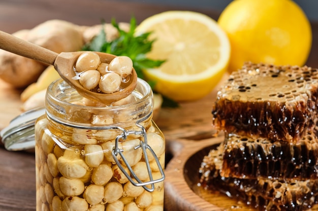 Honey in honeycombs on a wooden plate and golden honey in a jar with nuts and comb for honey with lemon and ginger