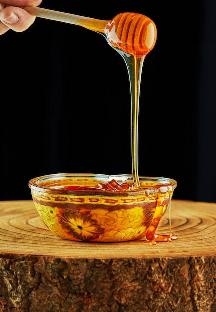 Honey is poured from a stick into an apple-shaped bowl on a wooden stand