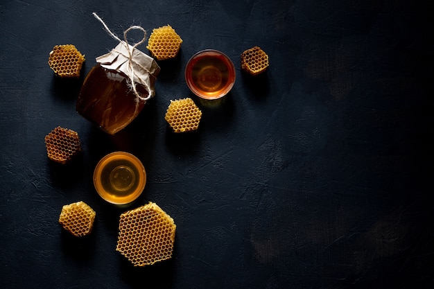 Photo honey in a jar and a honeycomb. on a black wooden background. free space for text. top view.