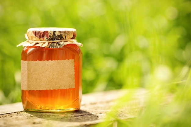 Honey jar with blank paper label on wooden table against green spring natural background