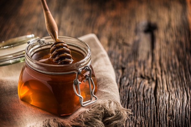 Honey jar with dipper on old woodn table.