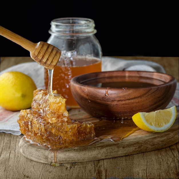 Honey in jar with honeycomb and wooden drizzler with lemon on wooden table. Dark background 