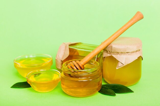 Honey in jar with leaves and honey dipper on colored background top view with copy text