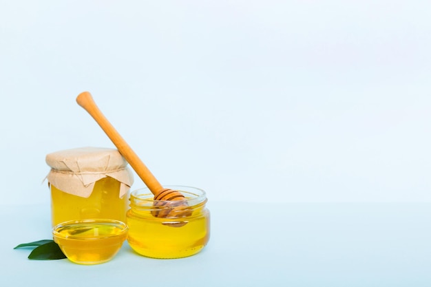 Honey in jar with leaves and honey dipper on colored background top view with copy text