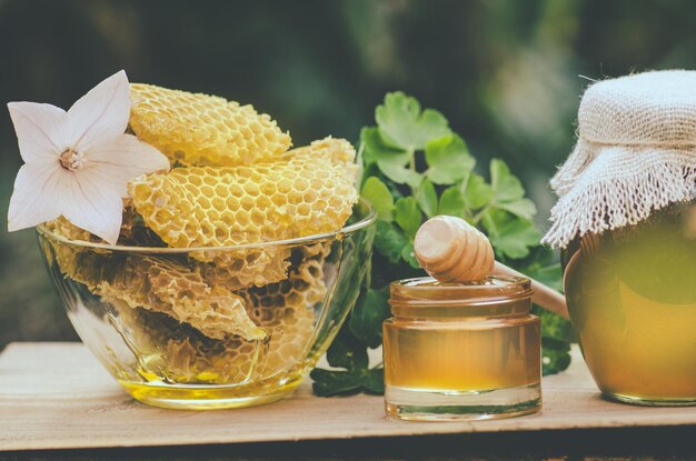 Honey jar and wooden stick on table against green blurred natural background Honey jar and honeycomb on wooden table outdoor Home made food