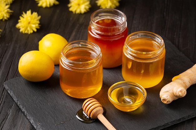 Honey in jars dipper lemon ginger on a dark background