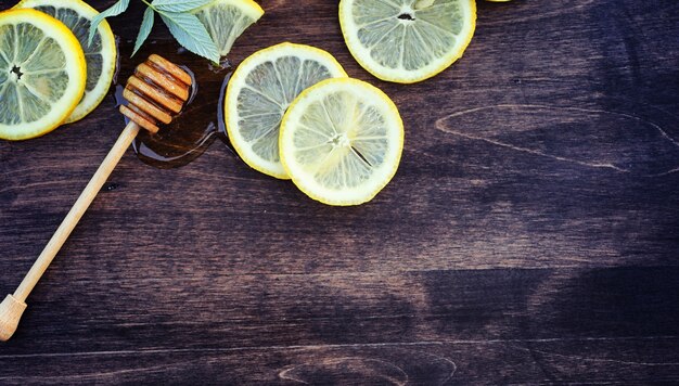 Miele e limone. bastone di miele e fette di limone a fette sul tavolo di legno. tè in tazza e miele di tiglio dolce in barattolo.