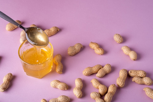 Honey liquid in glass with metal spoon with peanuts minimal on purple surface backdrop food nut texture copy space