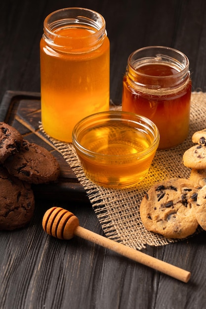 Honey in open jars and in a bowl dipper and homemade cookies with chocolate chips on a wooden background homemade cakes and honey for breakfast composition of craft chocolate cookies and honey