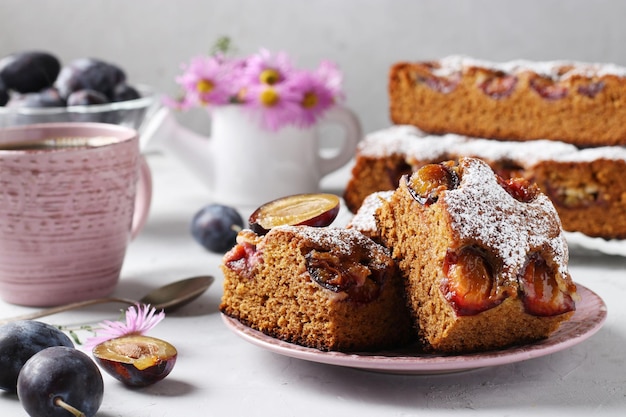 Honey pie with plums sprinkled with powdered sugar and cup of coffee on a light gray table