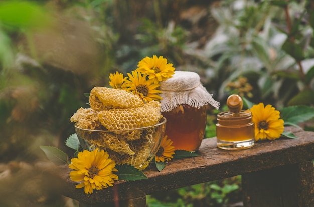 Photo honey pot, dipper, jar of fresh honey,  honeycomb on a wooden table outdoors. honey with honey dipper on wooden table