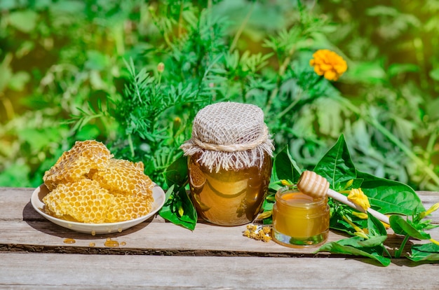 꿀 냄비, 국자, 신선한 꿀 항아리, 야외 나무 테이블에 벌집