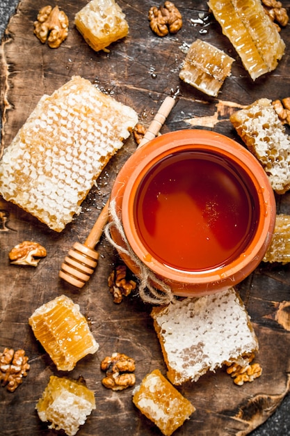 Honey pot and honeycomb with nuts on rustic table.