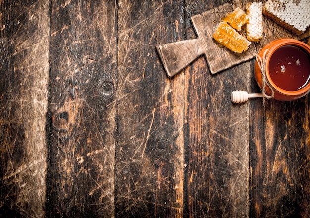 Honey pot and honeycomb with a wooden spoon on wooden table.