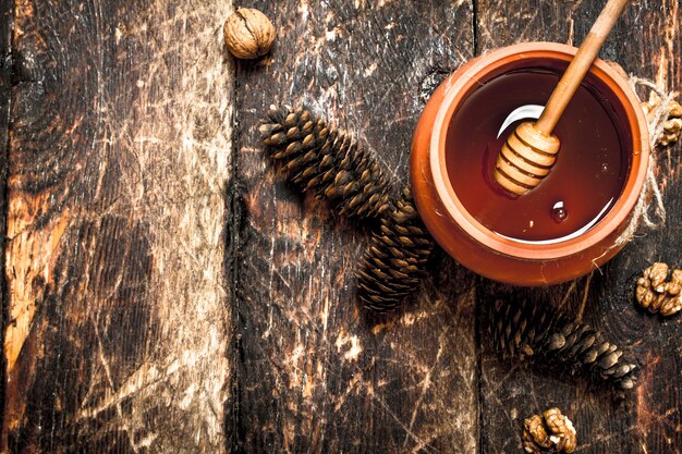 The honey in the pot with the nuts and cones on wooden table.