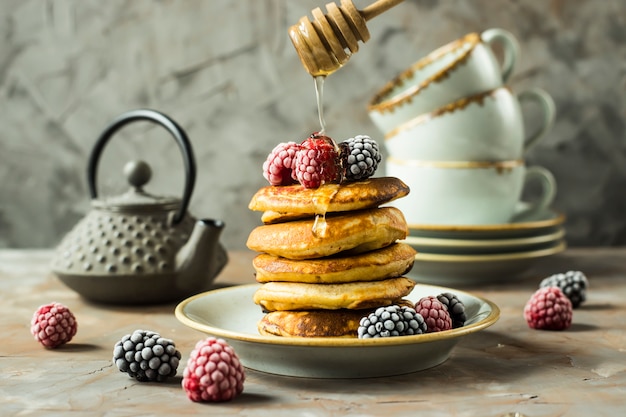 Honey pours on the drain of pancakes on a plate with raspberries and blackberries