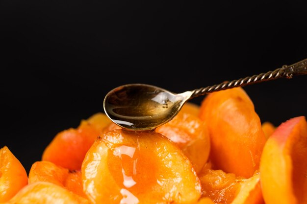 Honey pours from a spoon onto slices of juicy apricots on a black background