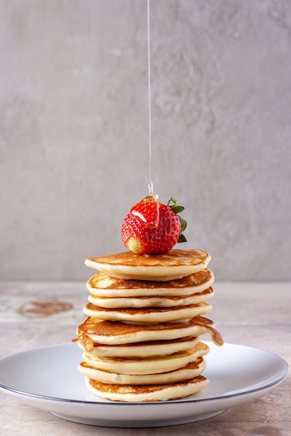 Honey pours on strawberries on a stack of pancakes