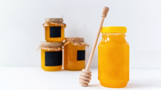 Honey products composition. Honey in a jars and special spoon. White wall