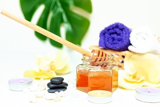 Honey spa treatment. Gold honey in a jar, orchid flowers, towels and scented candles. Natural home skin care.