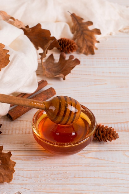 Honey, stick, jar, scarf, dry leaves. Rustic sweet autumn photo, white wooden background, copyspace.