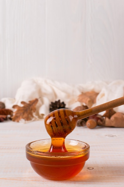 Honey, stick, jar, scarf, dry leaves. Rustic sweet autumn photo, white wooden background, copyspace.