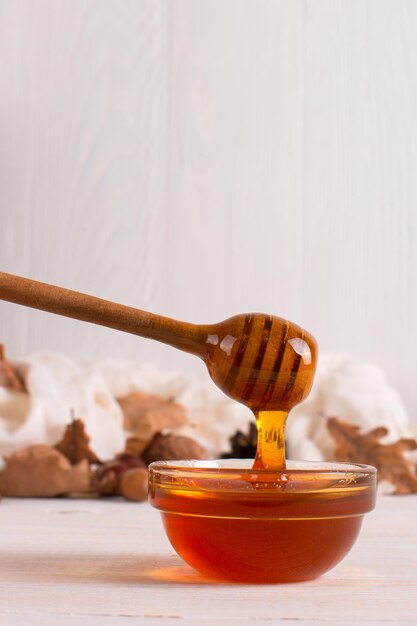 Honey, stick, jar, scarf, dry leaves. Rustic sweet autumn photo, white wooden background, copyspace.