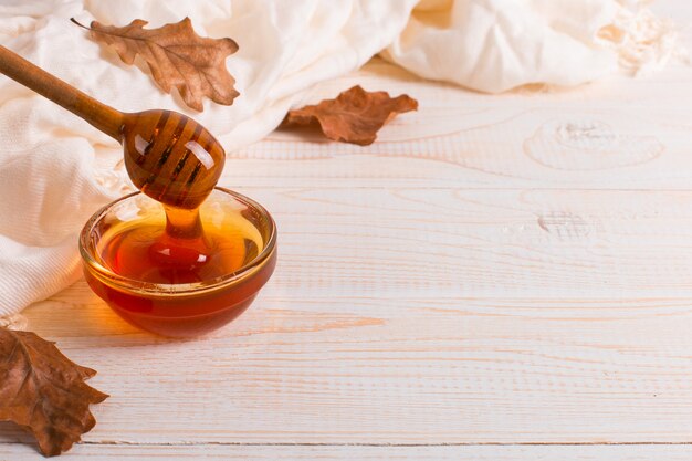 Photo honey, stick, jar, scarf, dry leaves. rustic sweet autumn photo, white wooden background, copyspace.