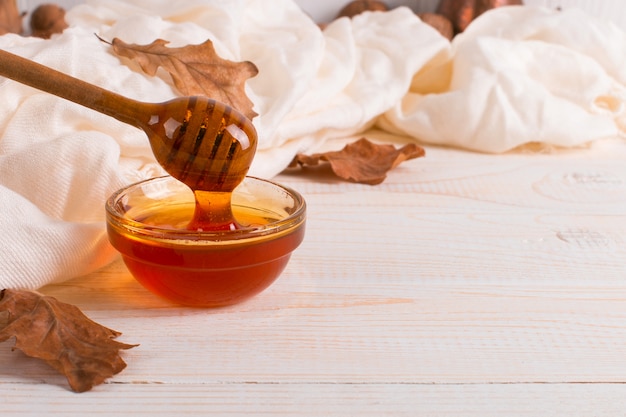 Honey, stick, jar, scarf, dry leaves. Rustic sweet autumn photo, white wooden background, copyspace.