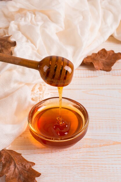 Honey, stick, jar, scarf, dry leaves. Rustic sweet autumn photo, white wooden background, copyspace.