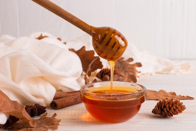 Honey, stick, jar, scarf, dry leaves. Rustic sweet autumn photo, white wooden background, copyspace.