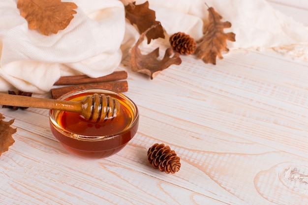 Honey, stick, jar, scarf, dry leaves. Rustic sweet autumn photo, white wooden background, copyspace.