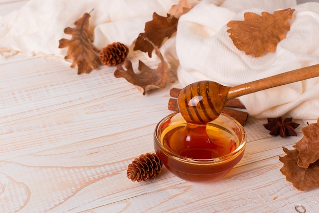 Honey, stick, jar, scarf, dry leaves. Rustic sweet autumn photo, white wooden background, copyspace.