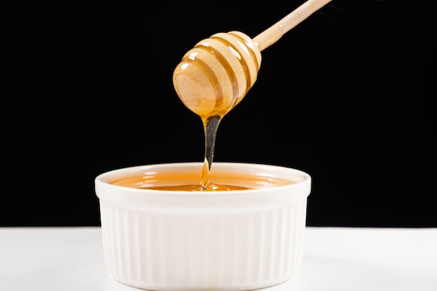 Honey in a white ceramic bowl with a wooden spoon on a black background