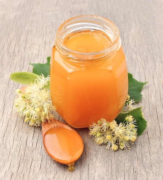 Honey with linden flowers on wooden texture.