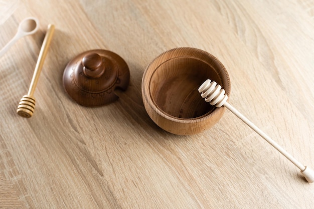 Honey with wooden honey dipper in wooden bowl on wooden table.