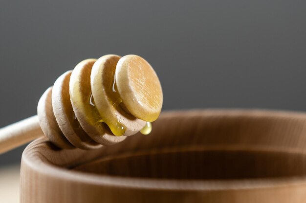 Honey with wooden honey dipper in wooden bowl on wooden table.