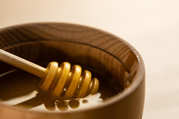 Honey with wooden honey dipper in wooden bowl on wooden table.