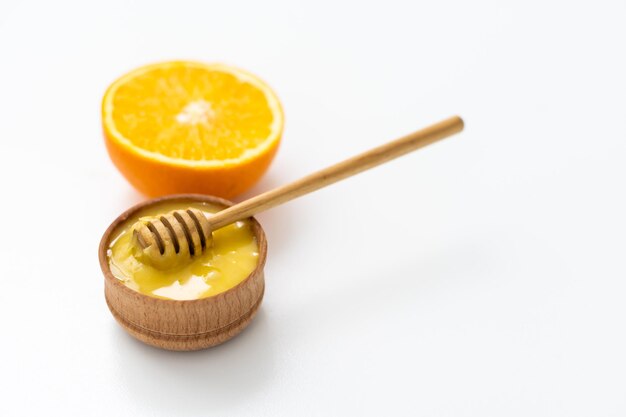 honey in a wooden bowl and orange on a white background.