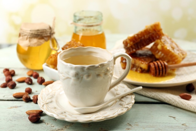 Honeycomb bowl with honey cup with herbal tea on color wooden table on light background